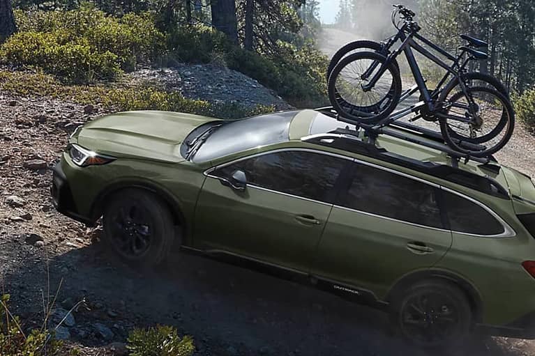 2022 Subaru Outback side angled view- driving up dirt road in forest area-bikes-green