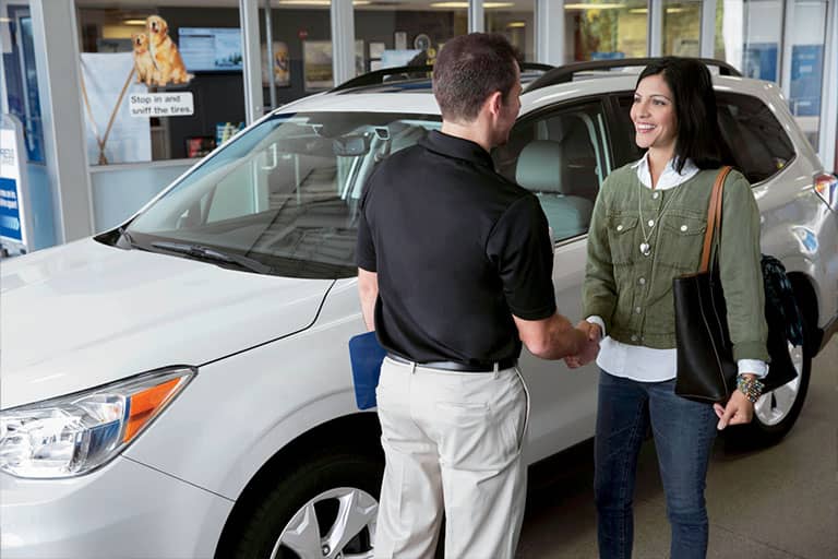 Man shaking hands with a female in front of a white Subaru vehicle.