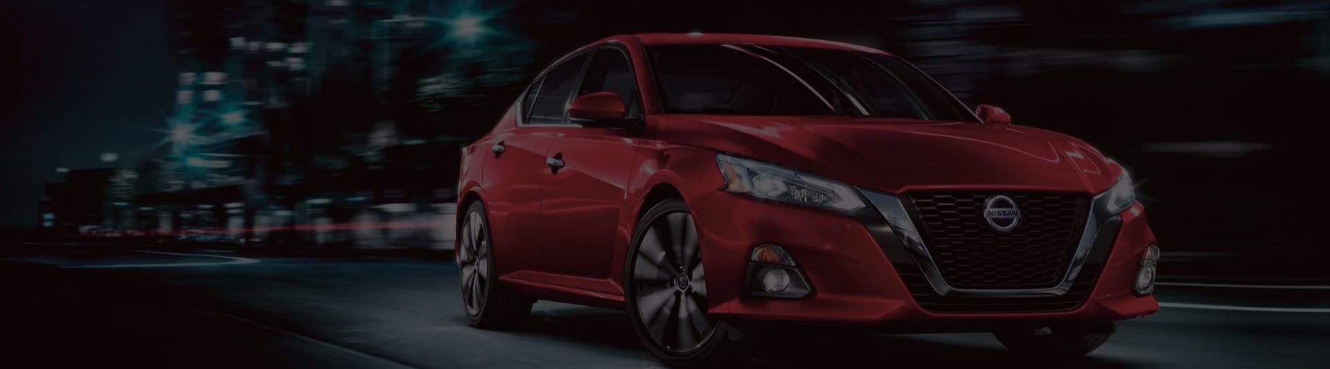 Red Nissan Altima driving through city at night