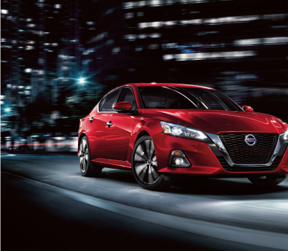 Front view of a red 2022 Nissan Altima driving through the city at night