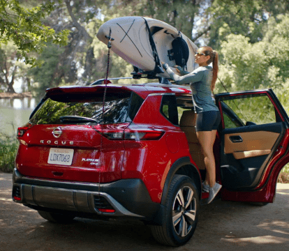 Woman putting a red kayak on the roof racks of a silver 2022 Nissan Rogue