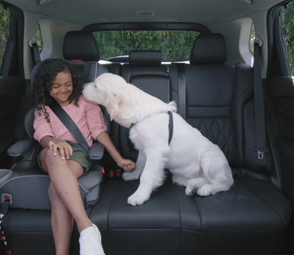 White dog kissing the face of a young girl in the backseat of a 2022 Nissan Rogue